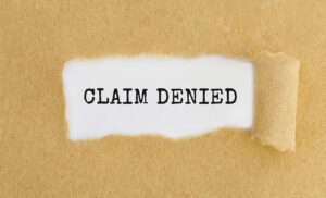 The text "claim denied" behind ripped brown paper